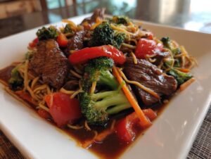 A close-up of a plate of 30 minute beef stir fry, featuring tender beef strips, broccoli florets, red bell peppers, and noodles in a savory sauce.