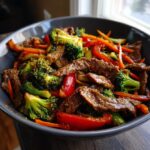 A close-up shot of a bowl filled with 30 minute beef stir fry, featuring tender beef strips, broccoli florets, sliced carrots, and red bell peppers.