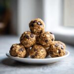 A stack of 5 ingredient energy balls studded with chocolate chips on a white plate.