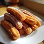 A close-up of a pile of golden-brown air fryer churros generously coated in sugar and cinnamon.