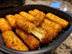 Close-up of golden brown air fryer mozzarella sticks, with one stick broken open to reveal melted, gooey cheese.