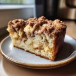 A delicious slice of moist apple coffee cake with a cinnamon crumble topping, served on a plate.