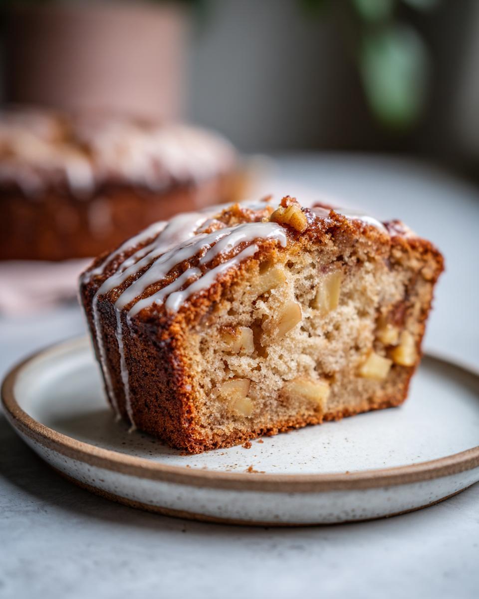 A close-up of a moist apple honey cake slice drizzled with white glaze and studded with apple pieces and nuts.