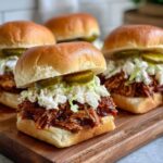 Close-up of BBQ pulled pork sliders topped with coleslaw and pickles on a wooden board.