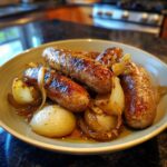 Close-up of beer braised bratwurst nestled in caramelized onions in a bowl.