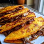 A plate of golden-brown birria tacos filled with tender shredded beef and melted white cheese.