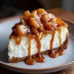 A slice of creamy caramel apple cheesecake drizzled with caramel sauce and topped with spiced apples.
