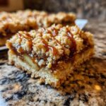 Close-up of a caramel apple pie bar with a crumbly topping drizzled with caramel sauce.