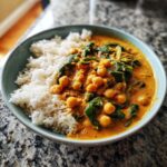 A close-up of a bowl of fluffy white rice served with a vibrant chickpea coconut curry and spinach.