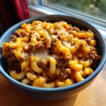 A close-up of a bowl filled with delicious chili mac and cheese, topped with melted cheddar.
