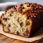 A close-up view of a moist chocolate chip banana bread loaf, showcasing the rich texture and abundant chocolate chips.