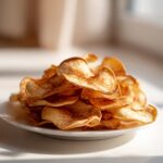 A pile of golden brown cinnamon apple chips dusted with cinnamon on a white plate, ready to be enjoyed.