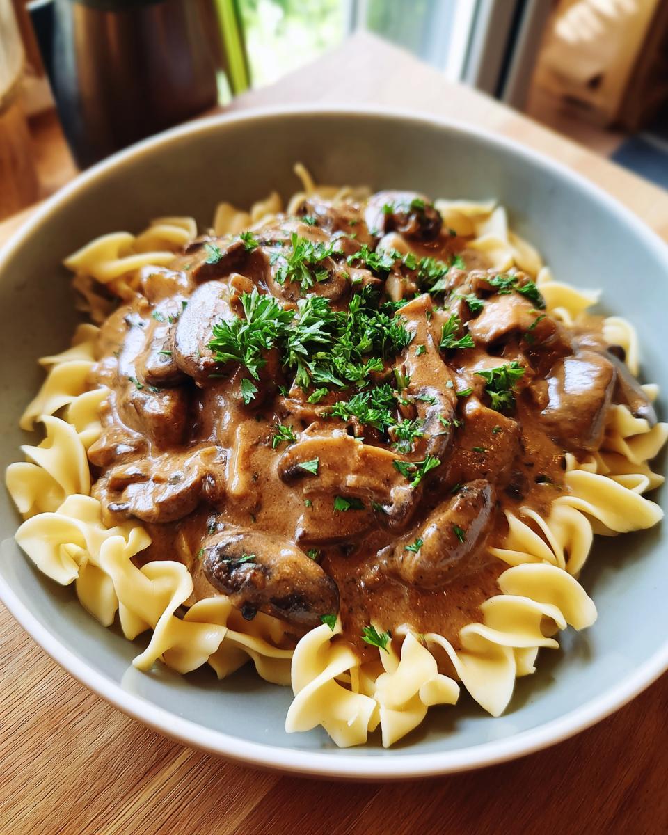 A bowl of creamy mushroom stroganoff served over wide egg noodles, garnished with fresh parsley.