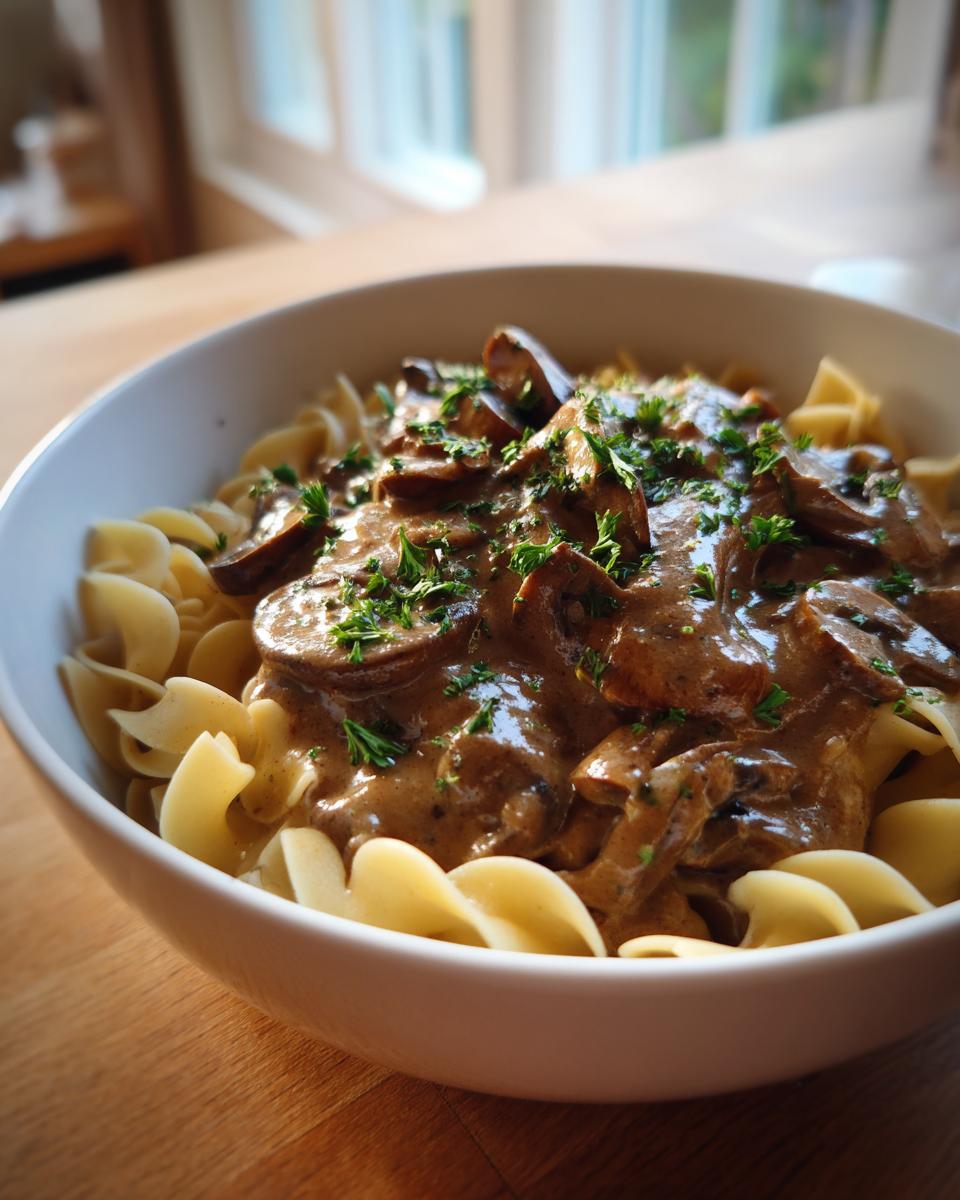 A bowl of creamy mushroom stroganoff served over egg noodles, garnished with fresh parsley.