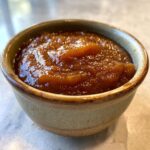 A close-up of rich, smooth crockpot apple butter served in a rustic ceramic bowl.