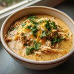 A close-up of a bowl of crockpot white chicken chili topped with shredded cheese and fresh cilantro.