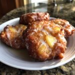Close-up of four golden brown easy apple fritters drizzled with white glaze on a white plate.