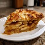 A close-up of a slice of easy apple pie on a white plate, showcasing the flaky crust and cinnamon-spiced apple filling.