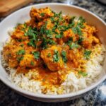 A bowl of fluffy white rice topped with tender pieces of easy butter chicken in a creamy orange sauce, garnished with fresh cilantro.