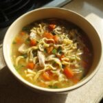 A close-up shot of a bowl of easy chicken noodle soup, featuring tender chicken, bright orange carrots, and wavy noodles in a savory broth.