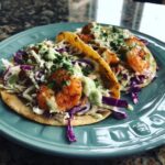 Two delicious easy shrimp tacos filled with seasoned shrimp, shredded cabbage, and a creamy sauce, garnished with cilantro.