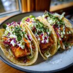 Three delicious fish tacos with crispy fish, colorful slaw, and creamy sauce, ready to eat.