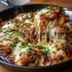 A spoonful of French onion chicken skillet with gooey melted cheese being lifted.