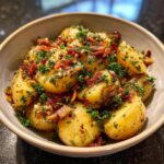 A close-up of a bowl filled with warm German potato salad, featuring tender potatoes, crispy bacon bits, and fresh parsley.