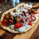 A close-up of a delicious Greek chicken gyros, filled with seasoned chicken, tomatoes, red onion, feta cheese, and tzatziki sauce on pita bread.