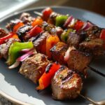 Close-up of juicy grilled steak kabobs with colorful bell peppers and red onion on a grey plate.