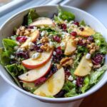 A close-up of a vibrant Harvest Apple Walnut Salad with fresh greens, apple slices, walnuts, dried cranberries, and feta cheese.