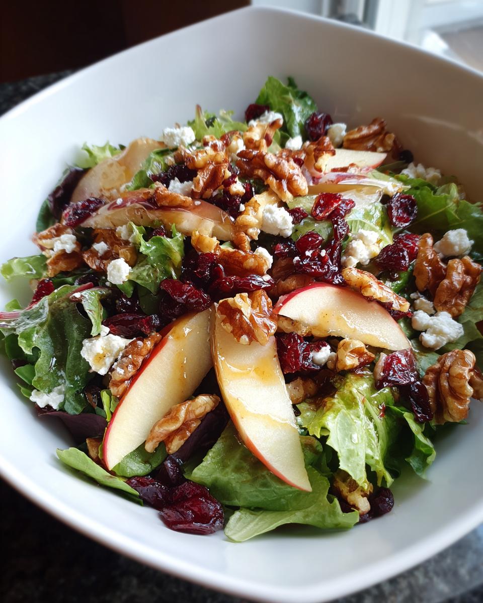 A close-up of a Harvest Apple Walnut Salad featuring crisp lettuce, apple slices, walnuts, dried cranberries, and crumbled feta cheese.