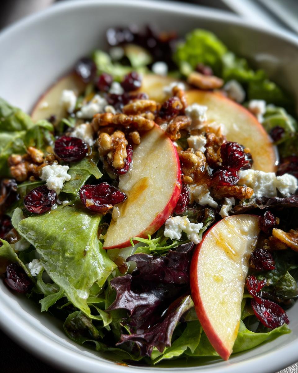 Close-up of a fresh Harvest Apple Walnut Salad with crisp lettuce, apple slices, walnuts, feta cheese, and dried cranberries.