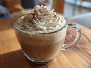 A close-up of a warm, homemade pumpkin spice latte in a clear mug, topped with whipped cream and cinnamon.