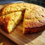 A slice of golden-brown Jalapeño Cheddar Cornbread on a wooden cutting board, showing visible cheese and green flecks.