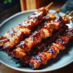 Close-up of juicy teriyaki chicken skewers, glazed and slightly charred, served on a grey plate.