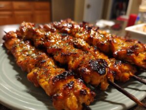 Close-up of several juicy teriyaki chicken skewers with a glossy glaze and sprinkled herbs on a light green plate.