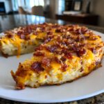 A slice of loaded baked potato casserole topped with melted cheddar cheese and crispy bacon.