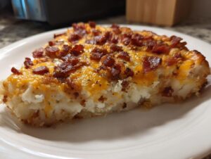 A close-up of a slice of loaded baked potato casserole topped with melted cheddar cheese and crispy bacon bits.