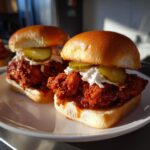Two delicious Nashville hot chicken sliders with spicy fried chicken, creamy slaw, and pickles on soft buns.