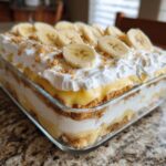 A close-up of a no bake banana pudding in a glass dish, topped with whipped cream and sliced bananas.
