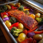 A perfectly cooked one pan salmon and veggies meal on a baking sheet, featuring seasoned salmon, potatoes, broccoli, and bell peppers.
