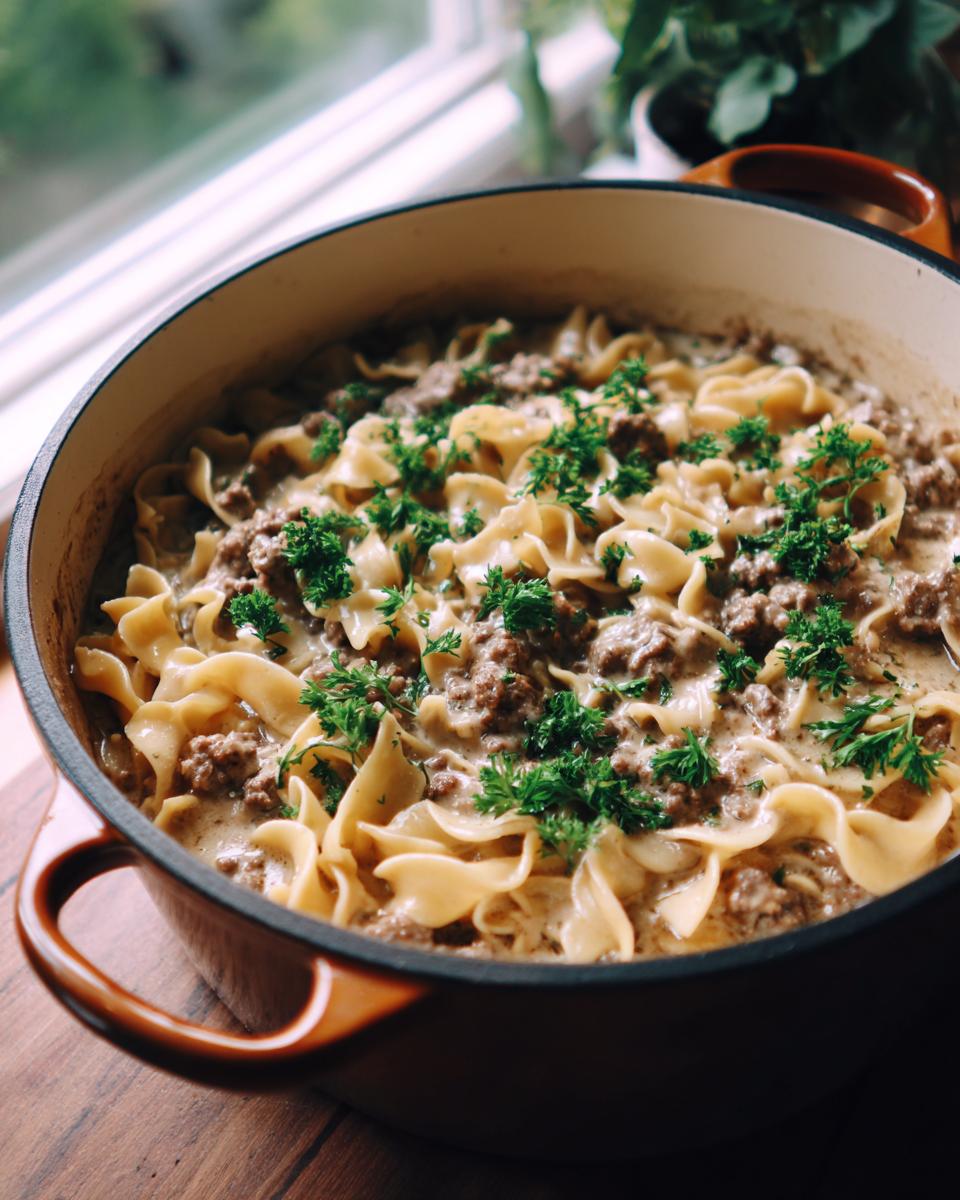 A close-up of a Dutch oven filled with creamy One Pot Beef Stroganoff and egg noodles, garnished with fresh parsley.