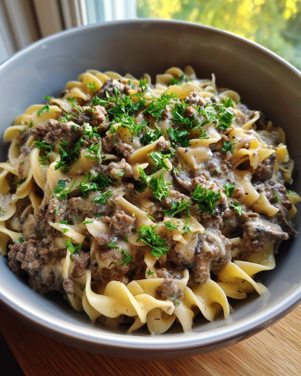 A close-up of a bowl of one pot beef stroganoff served over egg noodles and garnished with fresh parsley.