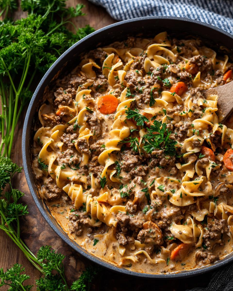 A close-up overhead view of a one pot beef stroganoff with tender egg noodles, ground beef, and sliced carrots in a creamy sauce, garnished with fresh parsley.