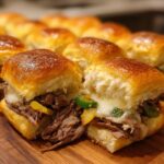 Close-up of two delicious Philly cheesesteak sliders filled with tender beef, melted cheese, and peppers on a wooden board.