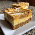 Close-up of a slice of pumpkin cheesecake bars with a graham cracker crust and swirled pumpkin and cream cheese filling.