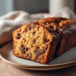 Close-up of two moist slices of pumpkin chocolate chip bread on a plate, showcasing abundant chocolate chips.