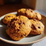 Close-up of several delicious pumpkin chocolate chip cookies on a plate, with chocolate chips visible.