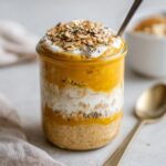A close-up of pumpkin pie overnight oats layered in a glass jar, topped with yogurt, oats, and cinnamon.